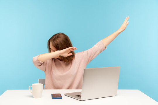 Dabbing trends. Overjoyed woman showing dab dance gesture, performing internet meme of success, sitting at workplace with laptop, home office job. indoor studio shot isolated on blue background