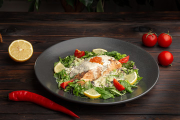 salmon steak in white sauce with red caviar and fresh vegetables in a round plate