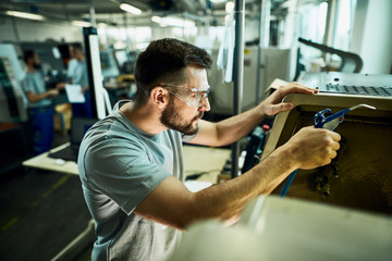 Young manual worker working with CNC machine in a factory.
