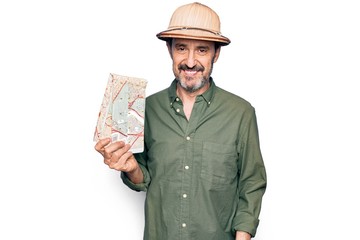Middle age handsome tourist man on vacation wearing explorer hat holding city map looking positive and happy standing and smiling with a confident smile showing teeth