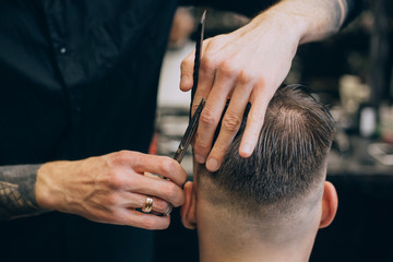 Young hipster man with hearty beard cutting his hair in a barbershop. Professional hairdressing work. Lifestyle