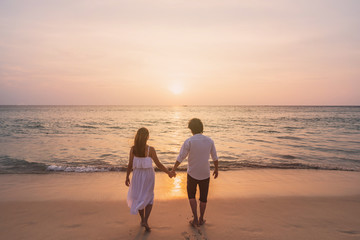 Fototapeta na wymiar Young woman traveler holding man's hand and looking beautiful sunset on the beach, Couple on vacation in summer concept
