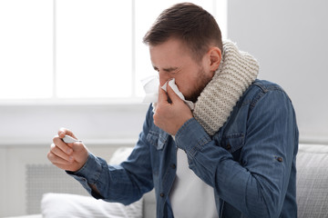 Sick man with fever blowing his runny nose at home