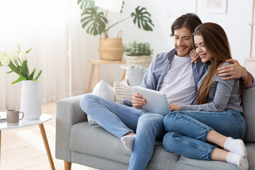 Fototapeta na wymiar Positive couple shopping online at home, using digital tablet