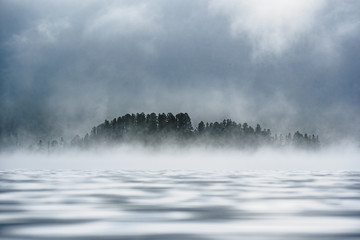 Fog-covered forest on the shore of a mountain lake in the Ulagansky District of the Altai republic, Russia