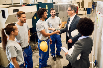 Happy company manager greeting with African American worker while visiting a factory.