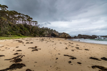 Rocks at the beach of the Mystery Bay in New South Wales, Australia at a cloudy and windy day in summer with strong waves in the ocean. 