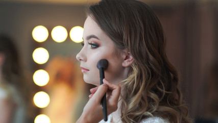 Makeup artist applies powder on the face of a 16 year old girl.