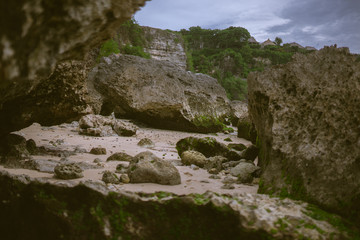 Beautiful deserted beach on the island of Bali at sunset. Rocks and nature. Plants and houses on the coast. Tropical paradise. Stones and white sand on the ocean