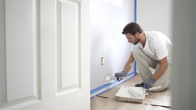 Painter with gloves painting the wall edge with brush. Handy painting above molding, baseboard.
