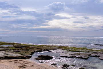 Beautiful deserted beach on the island of Bali at sunset. Rocks and nature. Plants and houses on the coast. Tropical paradise. Stones and white sand on the ocean