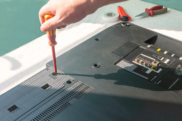 The specialist repairs the LCD TV at the workplace. A screwdriver in hand unscrews the lid of a...