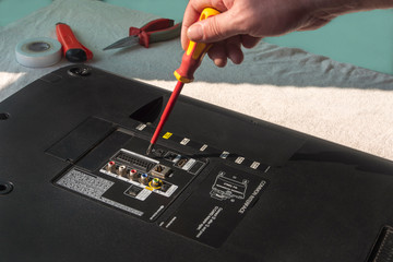 The master repairs the LCD TV, with an insulated screwdriver, removes the lid of the TV. Workplace...