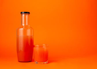 Bottle of grapefruit or orange juice and an glass cup on an orange background. Healthy eating concept. Minimalism
