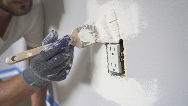 Close up of painter hands with gloves painting the wall around power outlet.