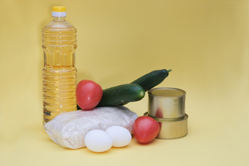 Crisis food stocks for the period of quarantine isolation on a yellow background. Rice, cucumbers, canned food, tomatoes, butter, chicken eggs. Food delivery, coronavirus quarantine. Copyspace.