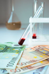 Money with laboratory flasks with blood on the table