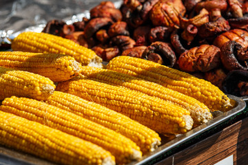 A lot of cooked corn close up. Yellow corn on the table at the festival.Fried vegetables in a metal stand at the fair.