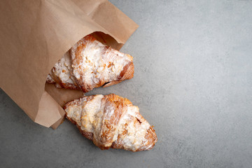 Freshly baked croissants in a package of craft paper on a grey tile background .