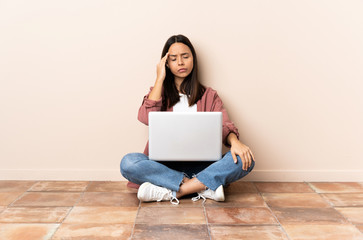 Young mixed race woman with a laptop sitting on the floor with headache