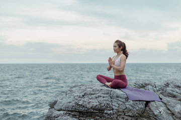 Fototapeta na wymiar Young woman practicing yoga. sitting in doing meditation exercise, Namaste hands Pose, Amazing yoga landscape in beautiful sky and enjoying sea view, concept for exercising, health care