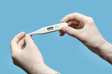 Hands in protective medical gloves hold a thermometer on a blue background.
