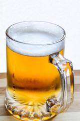 mug of fresh light beer on wood, back lit closeup