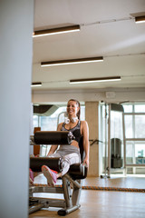 Fototapeta na wymiar Young woman having exercises on leg extension and leg curl machine in the gym
