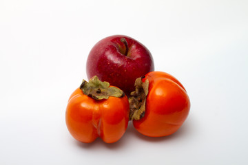 One red apple and two persimmons on a light background