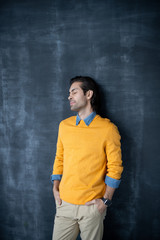 Tired young man in yellow sweater keeping eyes closed and holding hands in pockets while leaning on blackboard