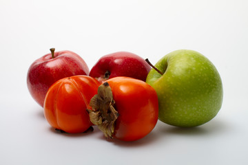 Three apples and two persimmons on a light background