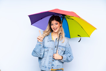 Teenager russian girl holding an umbrella isolated on blue background pointing up a great idea