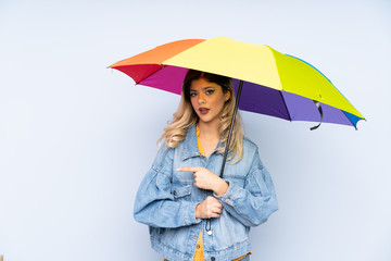 Teenager russian girl holding an umbrella isolated on blue background and pointing it