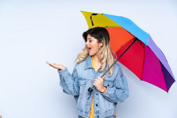 Teenager russian girl holding an umbrella isolated on blue background with surprise facial expression