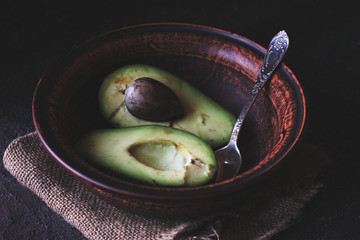 Green Avocado Halves With a Spoon in a Brown Clay Bowl on a Napkin