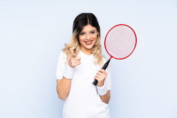 Teenager girl playing badminton isolated on blue background points finger at you