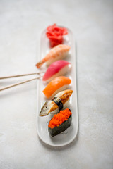 Plate with sushi rolls eel salmon shrimp tuna ginger and sticks on stone texture daylight restaurant