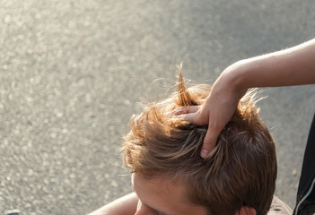 A girl does a head massage to her boyfriend on a city street. Hand in the hair. Relaxing head massage in the fresh air. Close-up photo of hand and head.