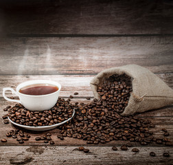 Hot coffee cups with smoke and coffee beans resting on a wooden background. A cup of hot coffee is served in the morning.