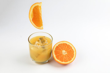 Fresh yellow orange juice in glass with whole floating sliced orange fruit and ice cube on white background