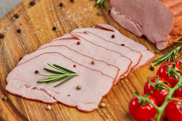 Sliced ham with spices, lettuce, avocado and tomatoes on wooden cutting board. Сold meat plate. Fresh prosciutto