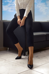 Low angle view of female legs in black breeches with large window on background