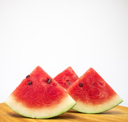 Watermelon with seeds sliced in a triangle shape, placed on a wooden surface, front view, close up, 