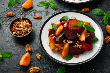 Vegan Plum, beet salad with pecan nuts, mint and herbs on rustic black table