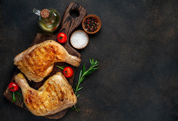 two grilled chicken legs with spices on a cutting board on a stone background with copy space for...
