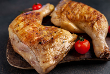two grilled chicken legs with spices on a cutting board on a stone background