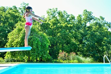 little girl with goggles on getting ready to jump into a swimming pool from a diving board