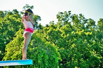 little girl with goggles on scared to jump into a swimming pool from a diving board