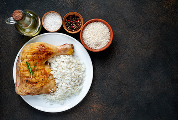 Grilled chicken leg with spices and rice on a white plate on a stone background with copy space for your text