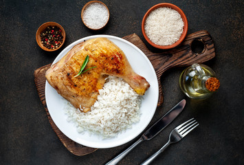 grilled chicken leg with spices and rice on a white plate on a stone background